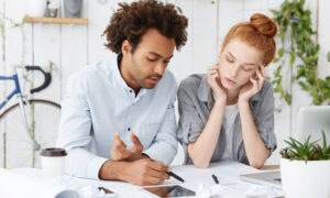 A man and women sitting at a table together, paying bills and their debt